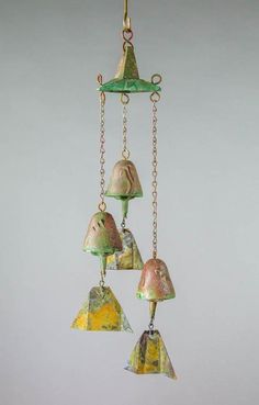 three glass bell ornaments hanging from chains on a white wall in front of a gray background