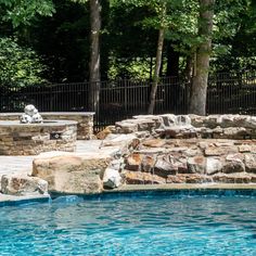 an outdoor swimming pool surrounded by stone walls and landscaping features is shown in this image