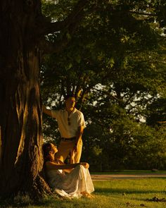 two people are sitting on the ground under a tree and one person is leaning up against it