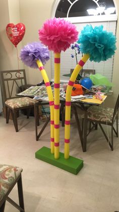 three tall poles with flowers on them are in the middle of a table and chairs