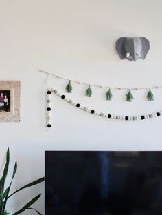 a flat screen tv sitting on top of a wooden table next to a wall hanging with tassels