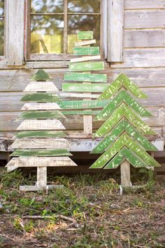 three wooden christmas trees sitting in front of a window on the ground next to grass