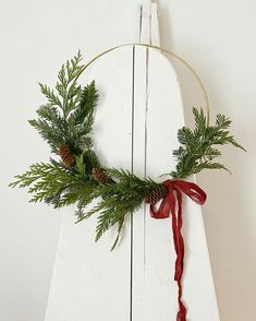 a wreath is hanging on the side of a white wooden structure with red ribbon and pine cones