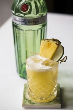 a pineapple margarita sitting on top of a table next to a bottle