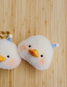 two white birds with blue beaks are on a wooden surface next to a gold heart