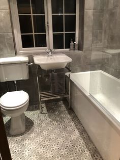 a white toilet sitting next to a bath tub and a sink in a bathroom under a window