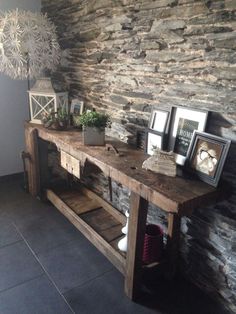 a wooden table sitting next to a stone wall with pictures on it and framed photos