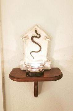 a glass bowl with a snake on it sitting on top of a wooden shelf next to a white wall