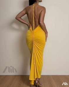 a woman in a yellow dress standing on a wooden floor with her back to the camera