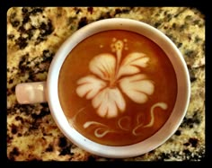 a cup of coffee with a flower painted on the foam in it sitting on a marble counter top