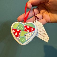 a hand holding a heart shaped ornament with a tag hanging from it's side