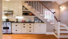 a kitchen with white cabinets and stairs leading to the upper floor, next to a stove top oven