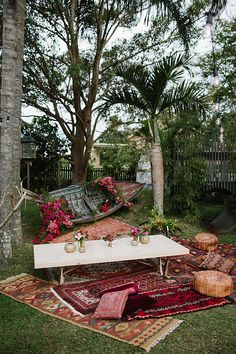 an outdoor area with rugs, tables and potted plants on the grass in front of trees