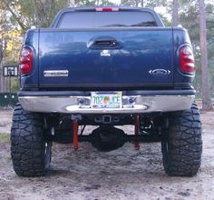 the back end of a blue pick up truck parked in a wooded area with trees