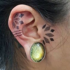 a woman with tattoos on her ear and behind the ear is a green leaf design