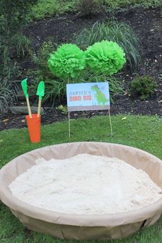 there is a sand pit in the grass with decorations around it and a sign that says dino dig