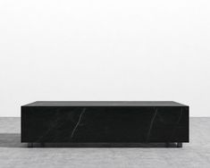 a black marble coffee table sitting on top of a cement floor next to a white wall