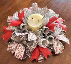 a candle sits on top of a wreath with red and white ribbon around it's edges