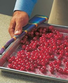 a person holding a knife over a pan filled with cranberries