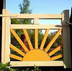 a wooden gate with the sun painted on it's side and trees in the background