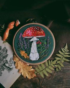 an embroidery project featuring a mushroom and leaves on a wooden table next to other items