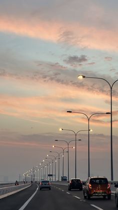 cars are driving down the highway at dusk with street lights and lamps on either side