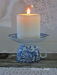 a lit candle sitting on top of a blue and white plate next to a lace doily