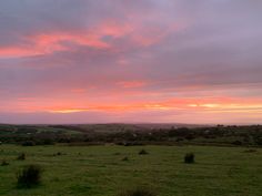 the sky is pink and orange as the sun sets in the distance over an open field