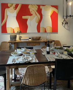 a dining room table is set with plates, bowls and utensils in front of a large painting