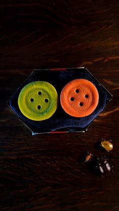 two orange and green buttons sitting on top of a wooden table next to an acorn