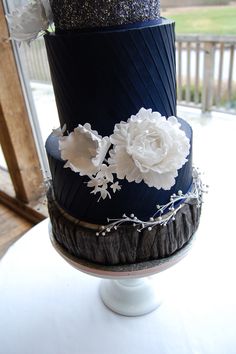 a three tiered cake with white flowers on the top and black icing, sitting on a table