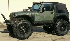 a green jeep is parked in front of a white building with black wheels and tires