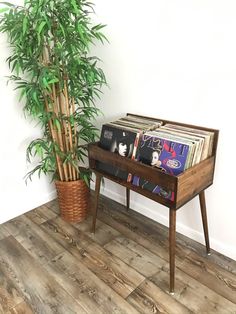 an old record player on a wooden stand next to a potted bamboo plant and vinyl records