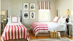 two beds in a bedroom with red and white bedding, striped rugs and pictures on the wall