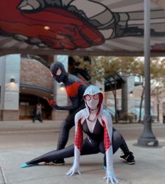 two people dressed as spider - man and black cat are on skateboards