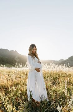 a pregnant woman wearing a white dress standing in a field