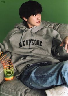 a young man sitting on top of a couch wearing a grey hoodie with the words we are one written on it