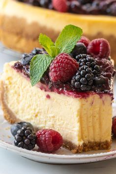 a cheesecake topped with berries and mint leaves on a plate next to another cake