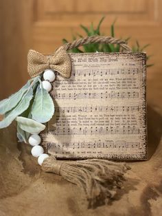 a wooden sign with white beads and a bow on top of it, next to a plant