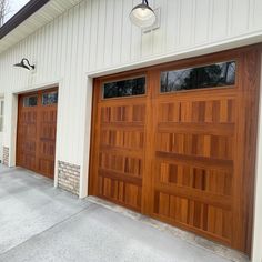 two brown garage doors in front of a white building with windows and lights on the side