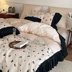 a bed with black ruffles and white sheets in a bedroom next to a night stand