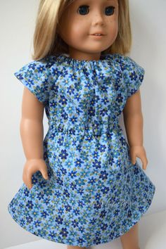 a doll with blonde hair wearing a blue floral dress and brown shoes, standing on a white surface