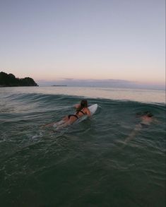 two people on surfboards in the water near an island and some hills at sunset