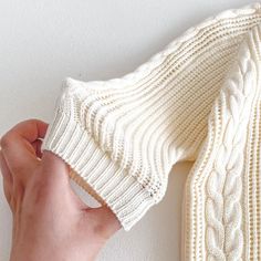 someone is holding the edge of a white knitted sweater over their left shoulder, with one hand on it