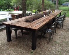 a wooden table with chairs around it in the middle of a gravel area next to trees