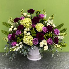 a white vase filled with lots of purple and green flowers on top of a table