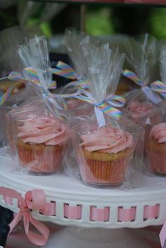 cupcakes with pink frosting and bows are on display in plastic wrappers