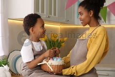 two women sitting on a kitchen counter, one holding a basket with eggs and the other holding flowers