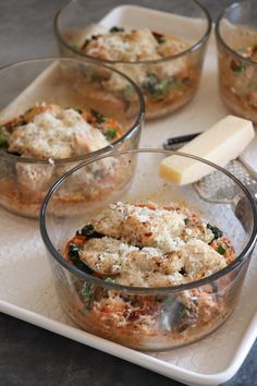 four glass bowls filled with food on top of a white tray next to a cheese wedge