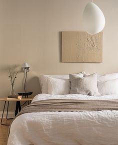 a bed with white linens and pillows in a bedroom next to a painting on the wall